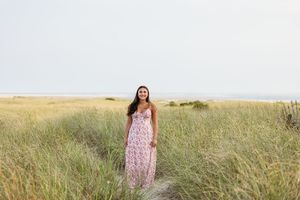 A person in a floral dress stands in a golden prairie field during sunset.