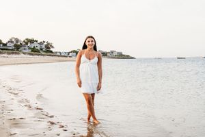 A person in a white dress walks along a pristine tropical beach with palm trees and turquoise water in the background.