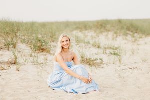 A person in a light blue dress sits gracefully on a sandy beach during golden hour.