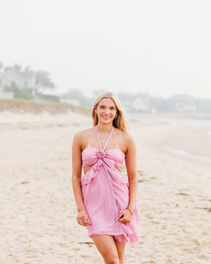 A person in a pink halter dress poses playfully on a sandy beach during a photo session.