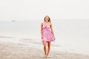 A woman in a pink dress walks along a sandy beach at sunset creating a dreamy coastal scene.