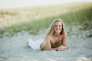 A person lying in soft beach sand wearing a white dress while posing at sunset.