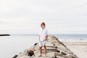 A person in white clothing poses on a large piece of driftwood at a serene beach during golden hour.