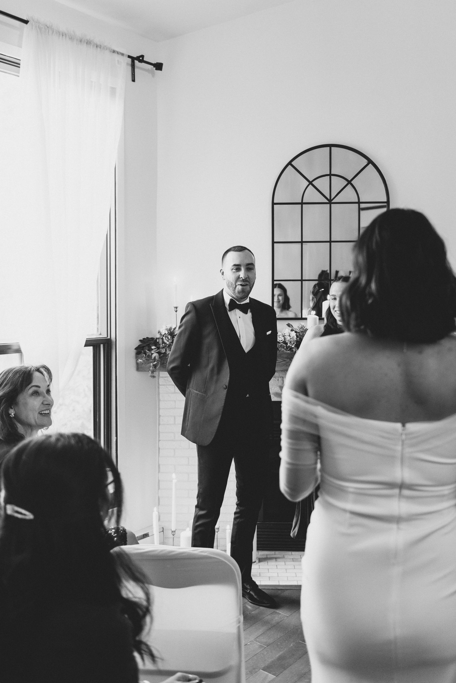 A black and white wedding scene shows a couple during their ceremony with an arched window in the background.