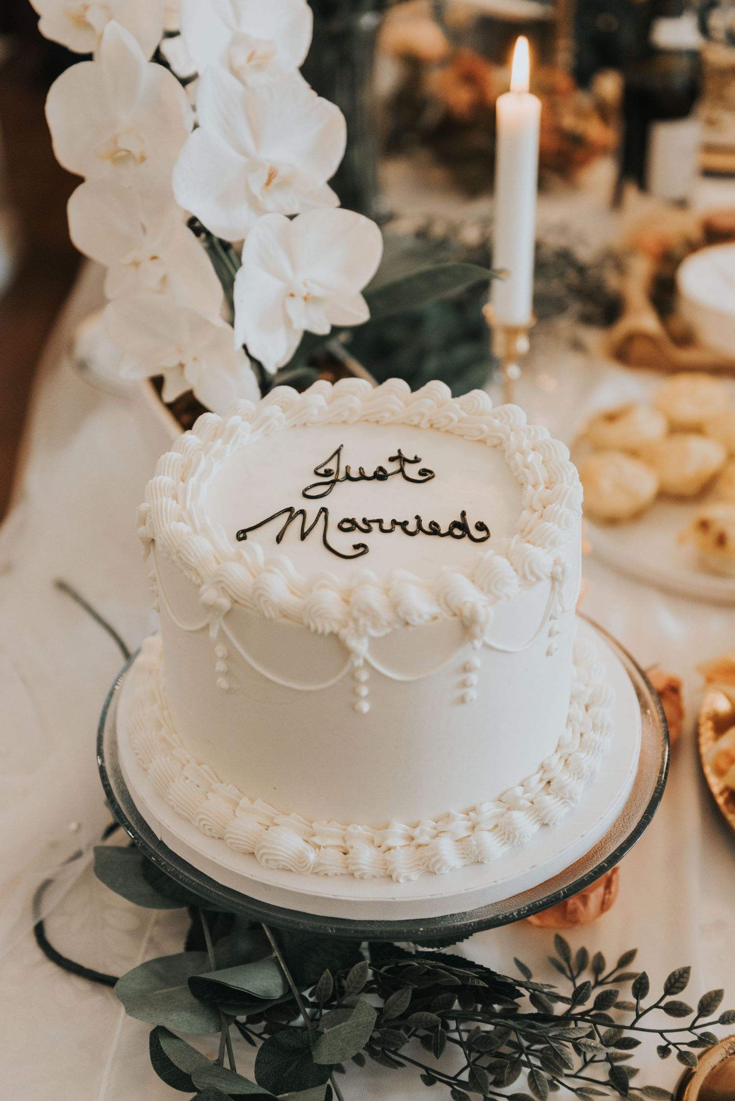 White wedding cake with elegant piped details and black foliage decorations displayed on a dessert table.