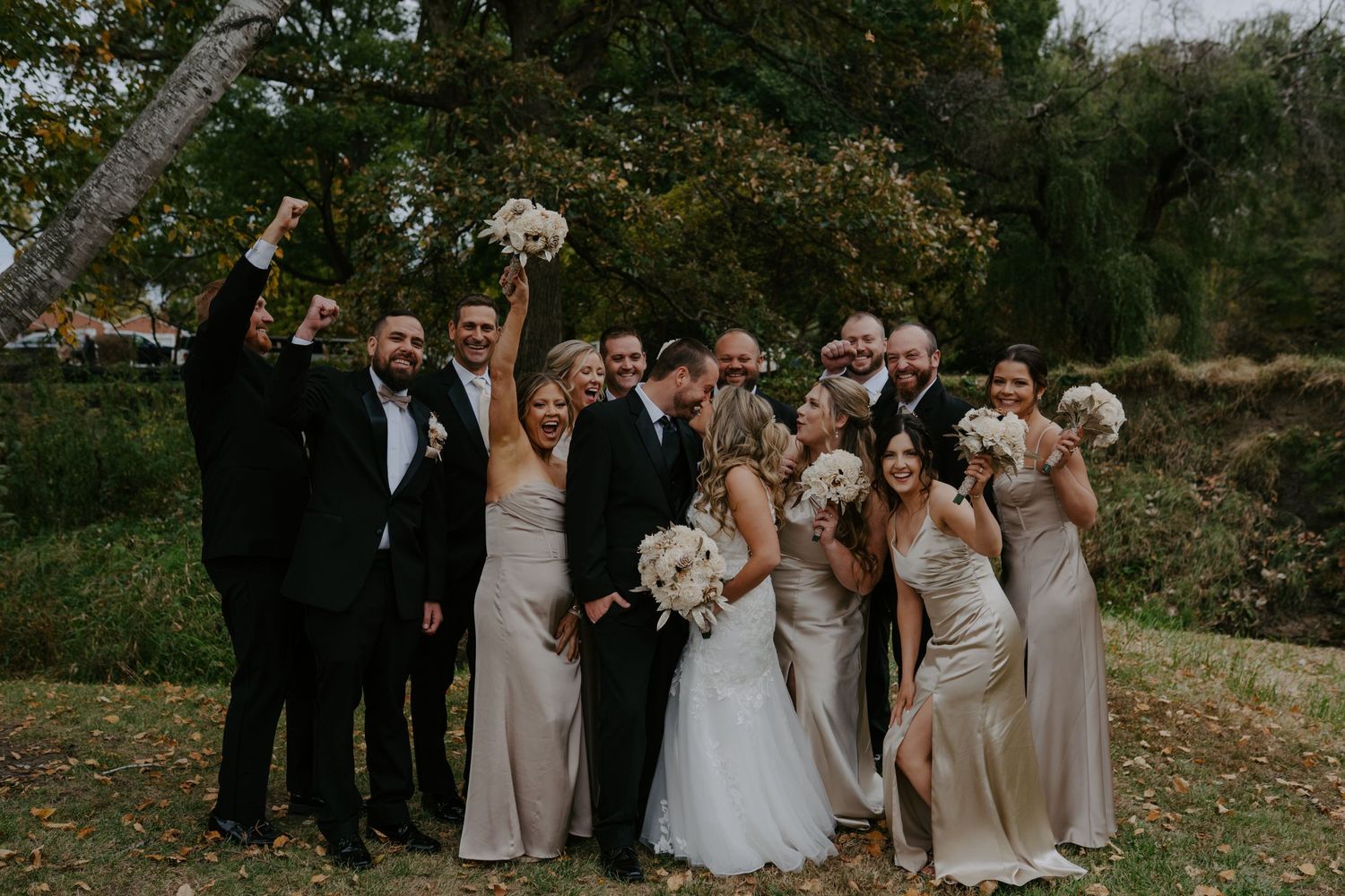 Wedding party celebrating outdoors in autumn with raised hands.