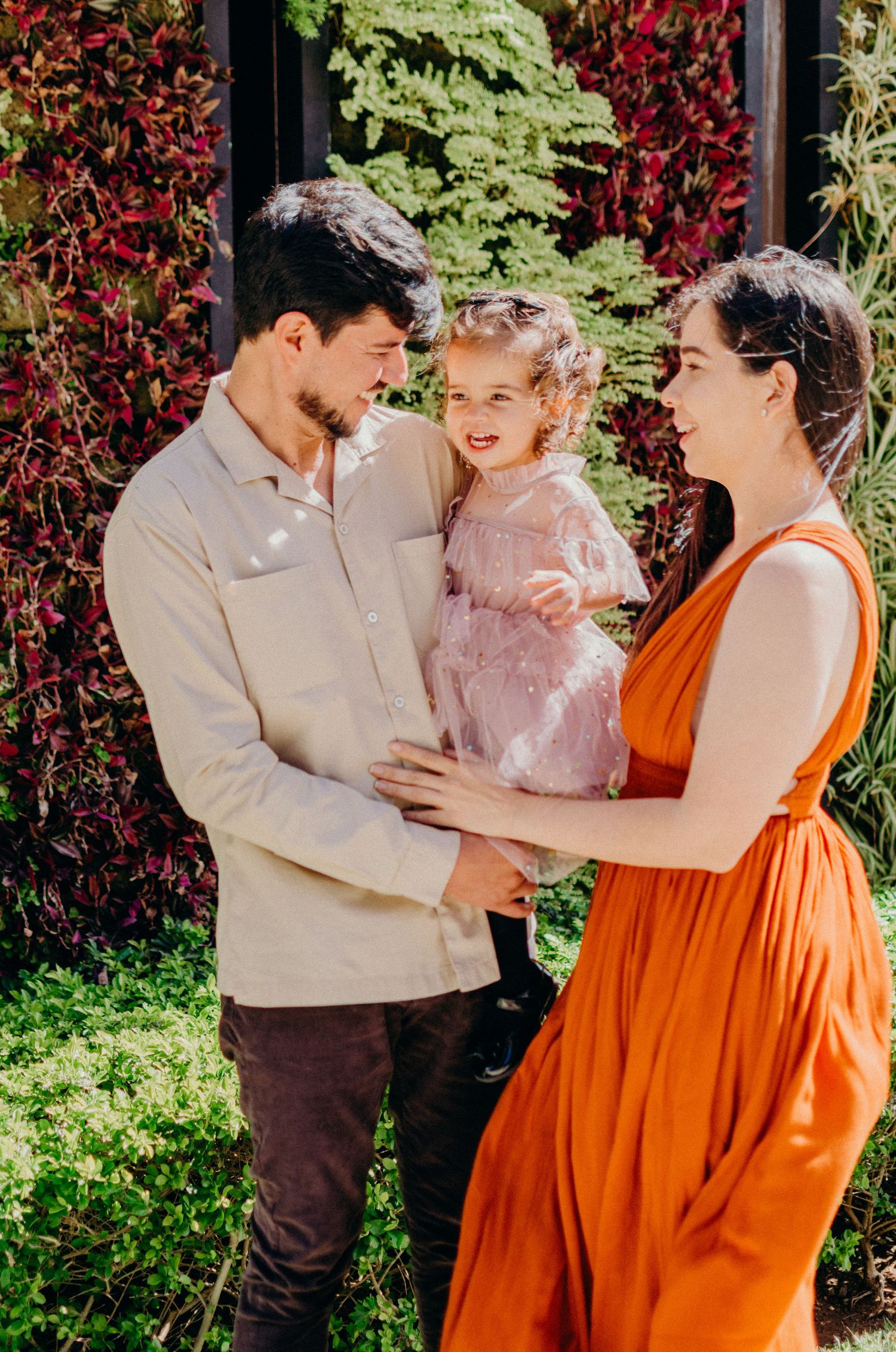 A family shares a joyful moment together against a backdrop of red and green foliage in their garden.