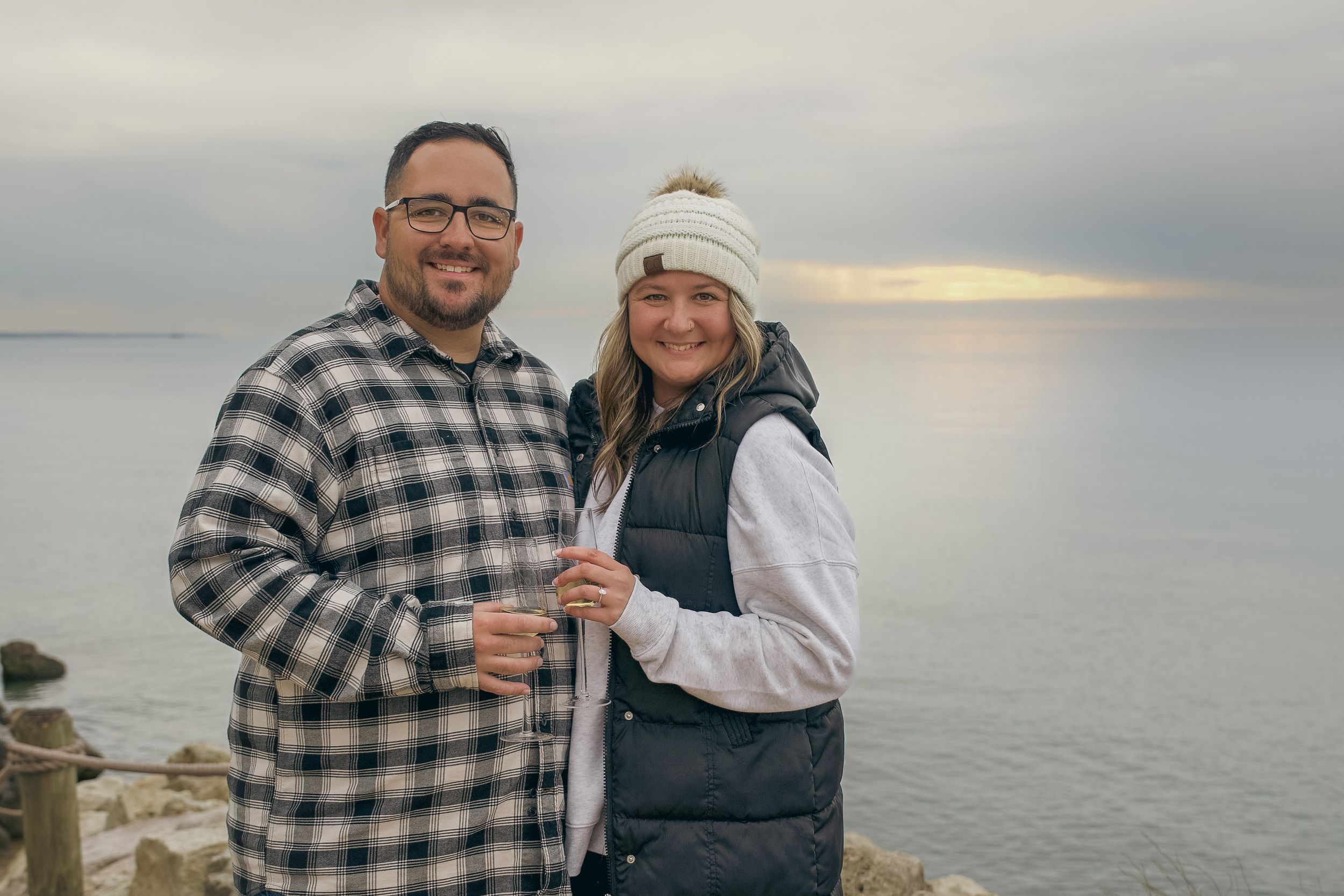 A couple shares a romantic moment at sunset along the rocky coastline with the ocean in the background.