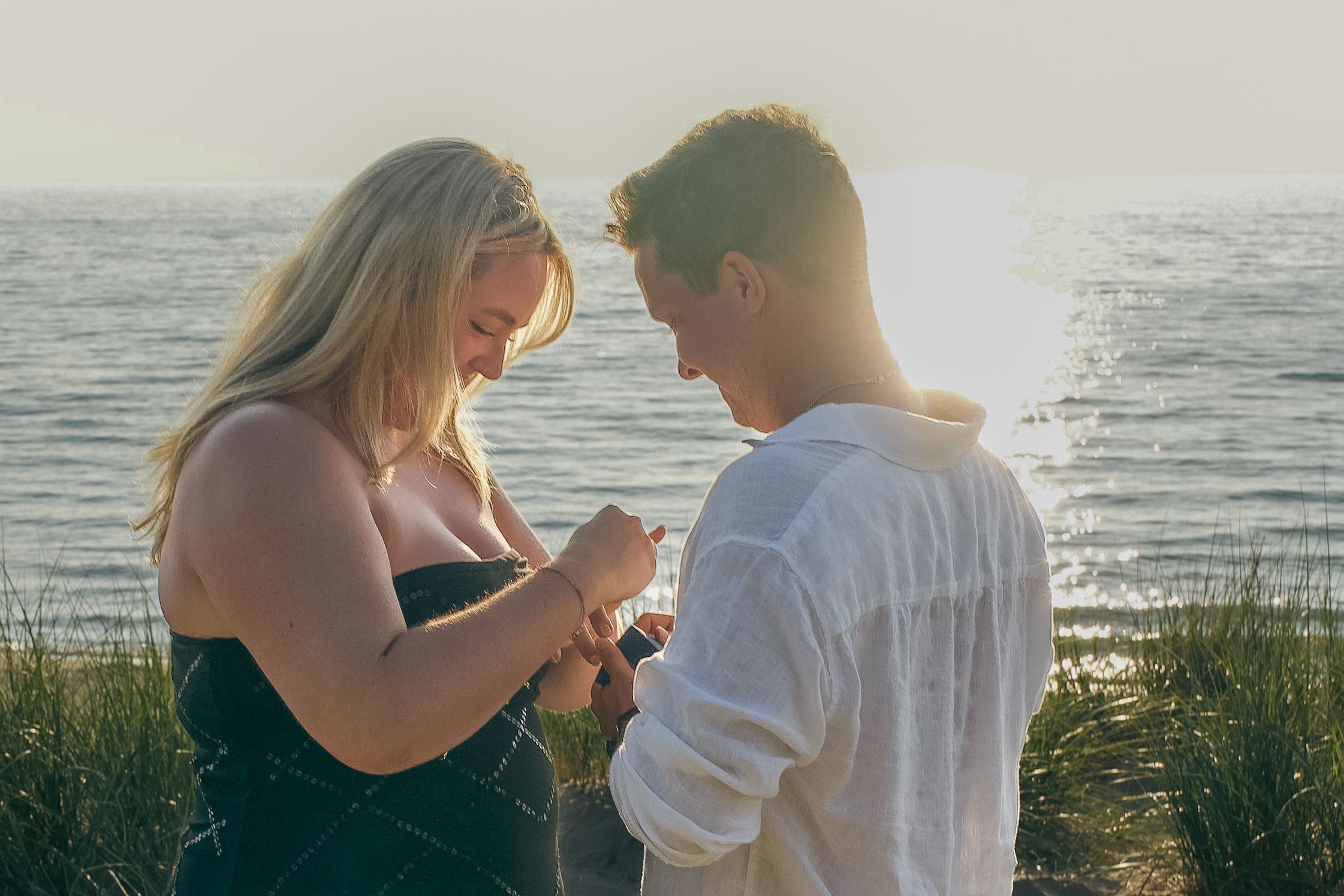 A couple stands silhouetted against a sunset beach backdrop during an intimate beachside moment.