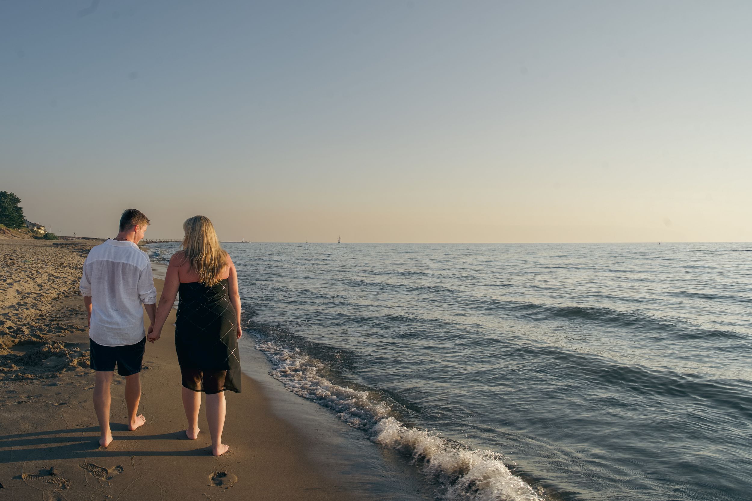 People walking along a beach shoreline at sunset with gentle waves rolling onto the sand.