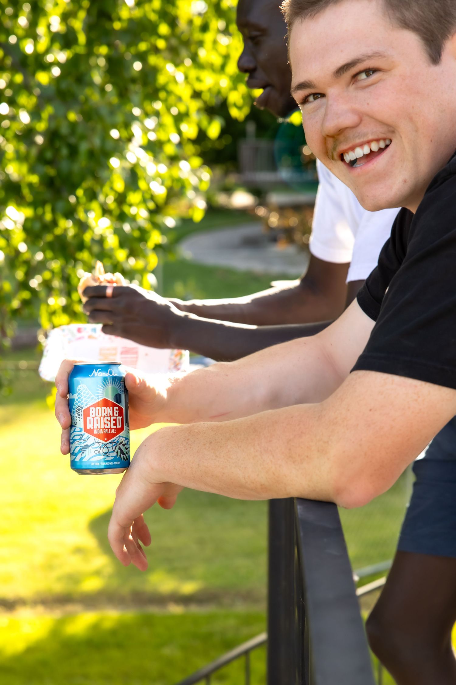 A can of Mountain Dew soda being held against a bright sunny outdoor background with trees.