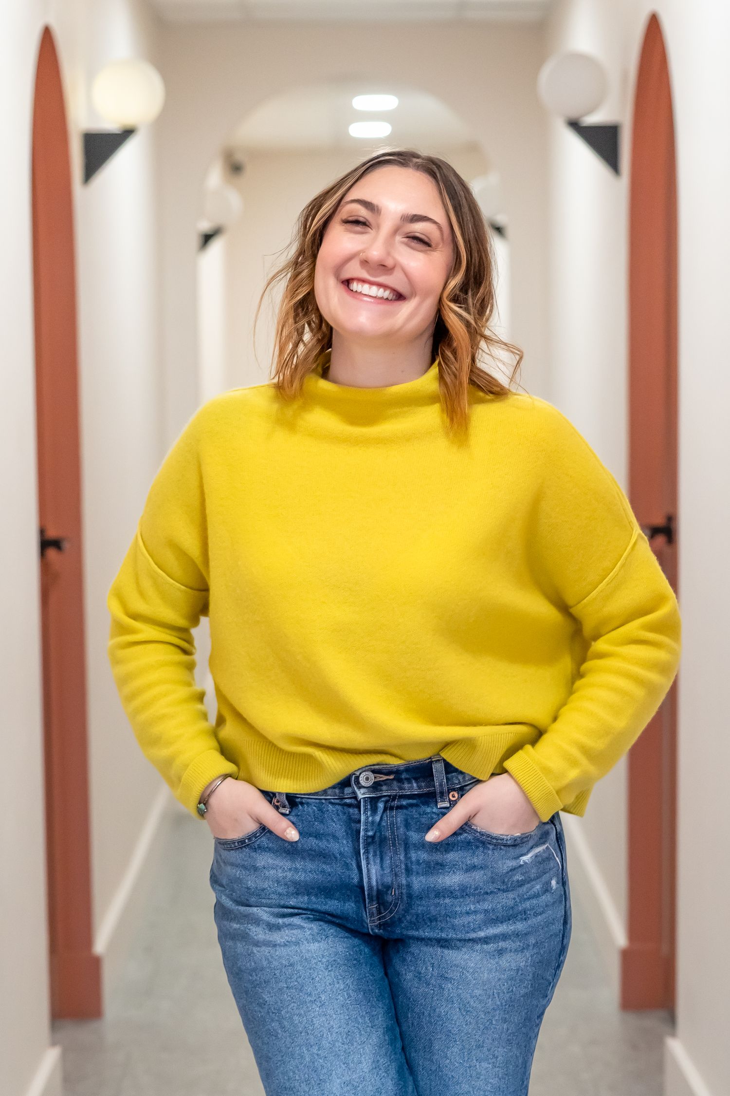 Four poses of someone wearing a bright yellow sweater and blue jeans standing against a white hallway background.