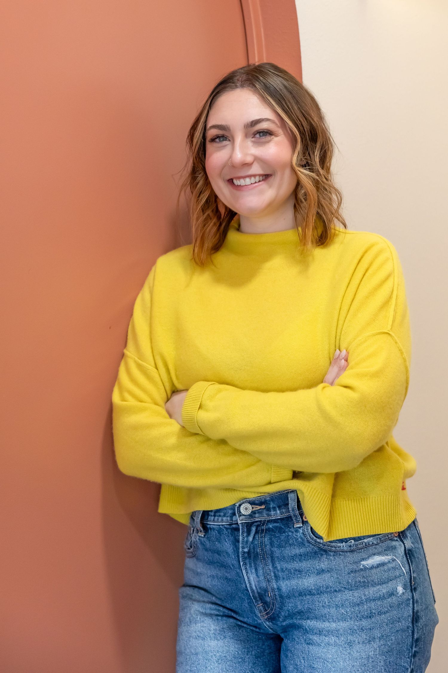 A series of photos showing someone in a bright yellow sweater and blue jeans posing with crossed arms against a pink wall.