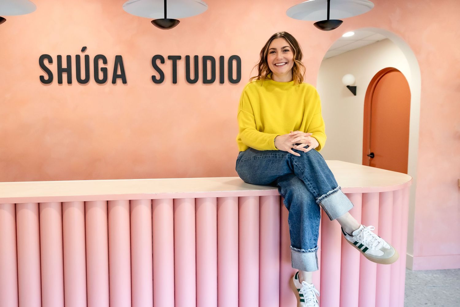 Pink and peach toned studio interior with modern radiator design and person sitting in yellow sweater.