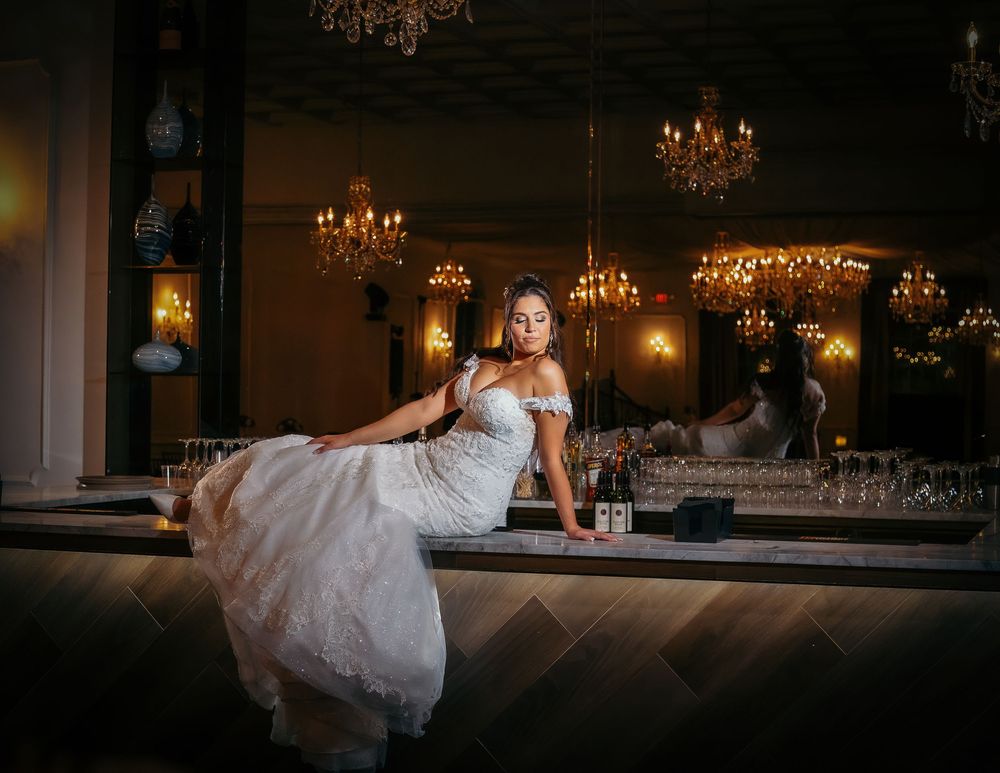 Wedding couple poses romantically on a bar counter in an elegant venue with warm lighting and chandeliers.