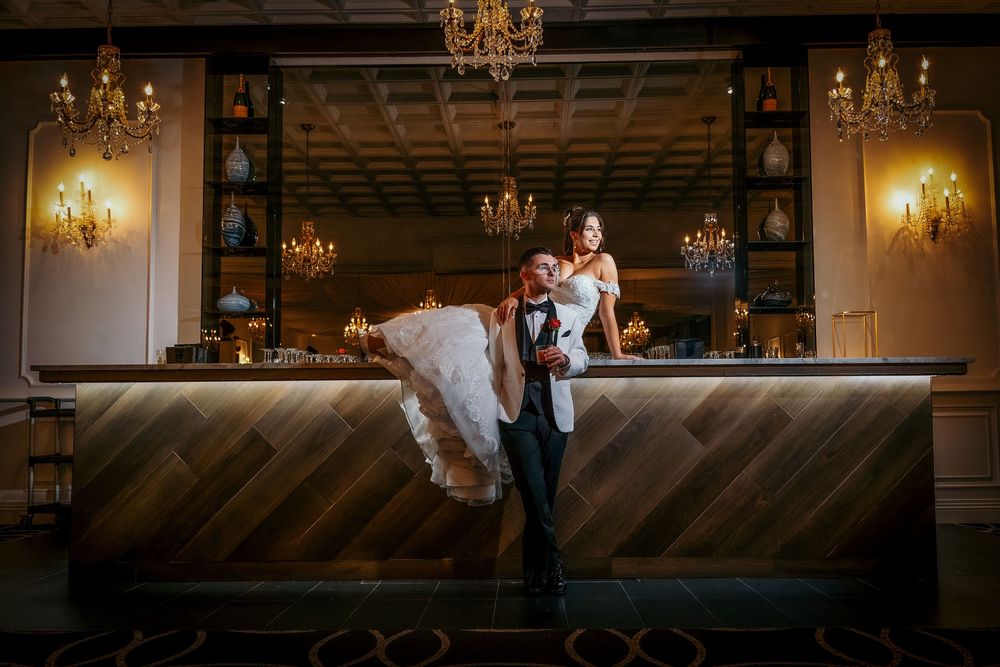 Couple shares romantic moment at elegant bar with crystal chandeliers and wooden accents in warm lighting.