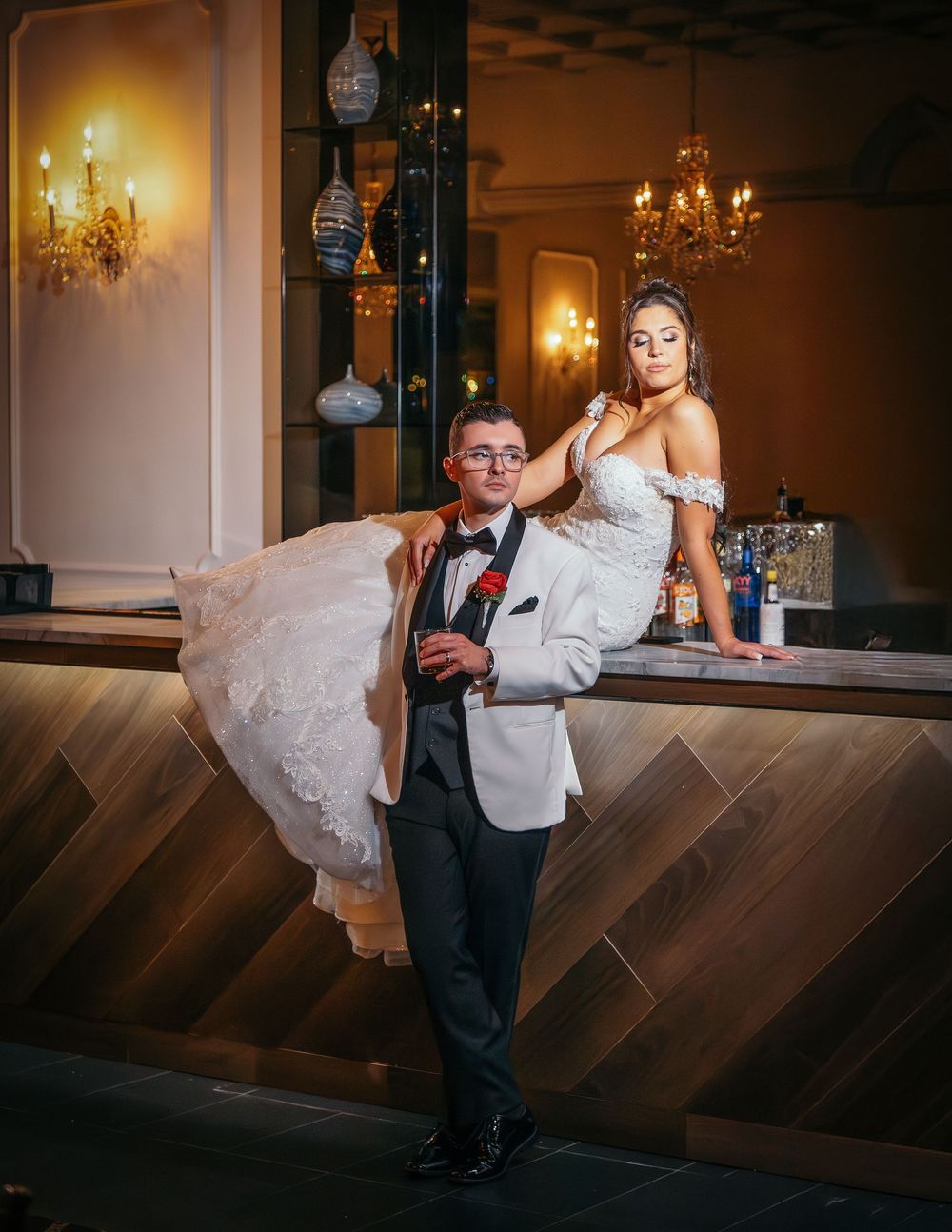 A couple performs an elegant dip dance move in a grand ballroom with chandeliers and warm lighting.