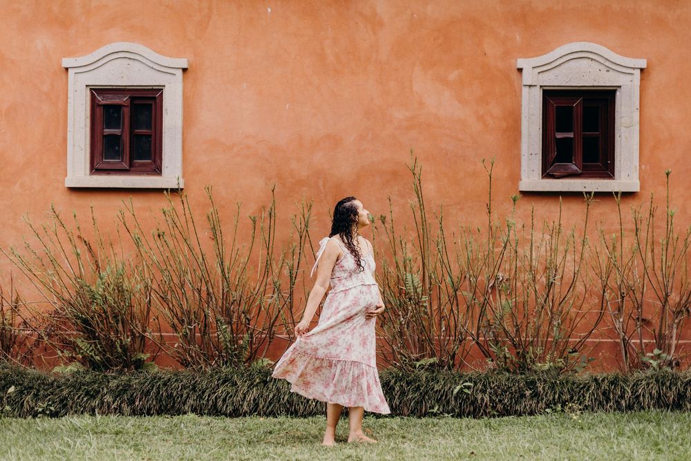 A white dress flows gracefully against a rustic orange wall with small windows.