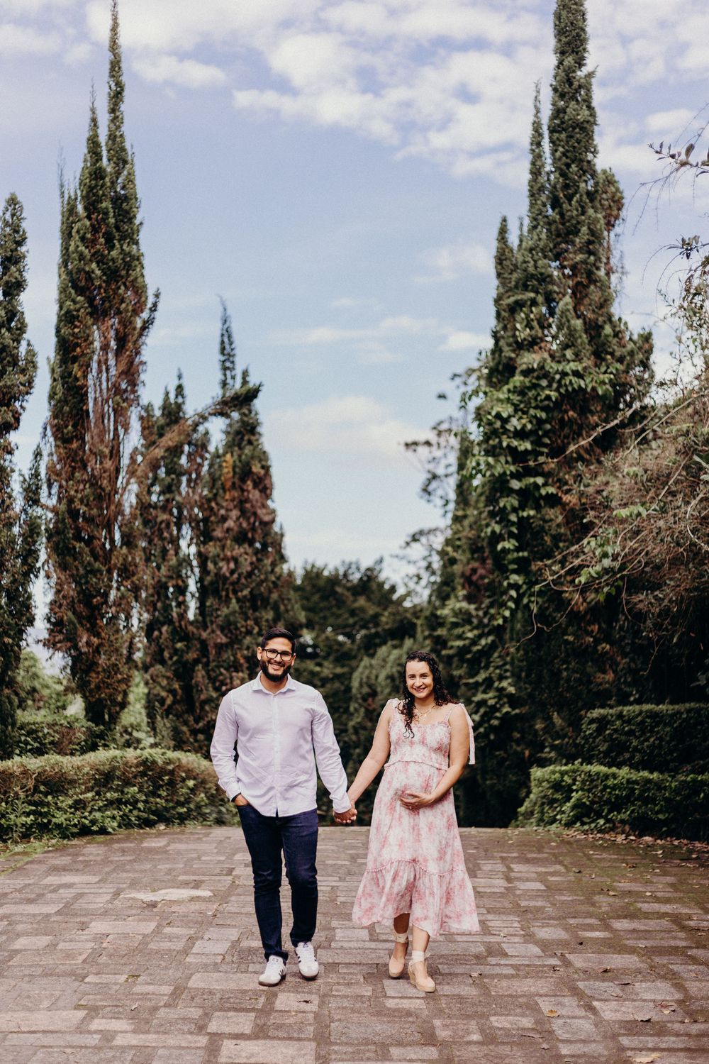 Couple walking together on stone patio surrounded by tall cypress trees on a sunny day.