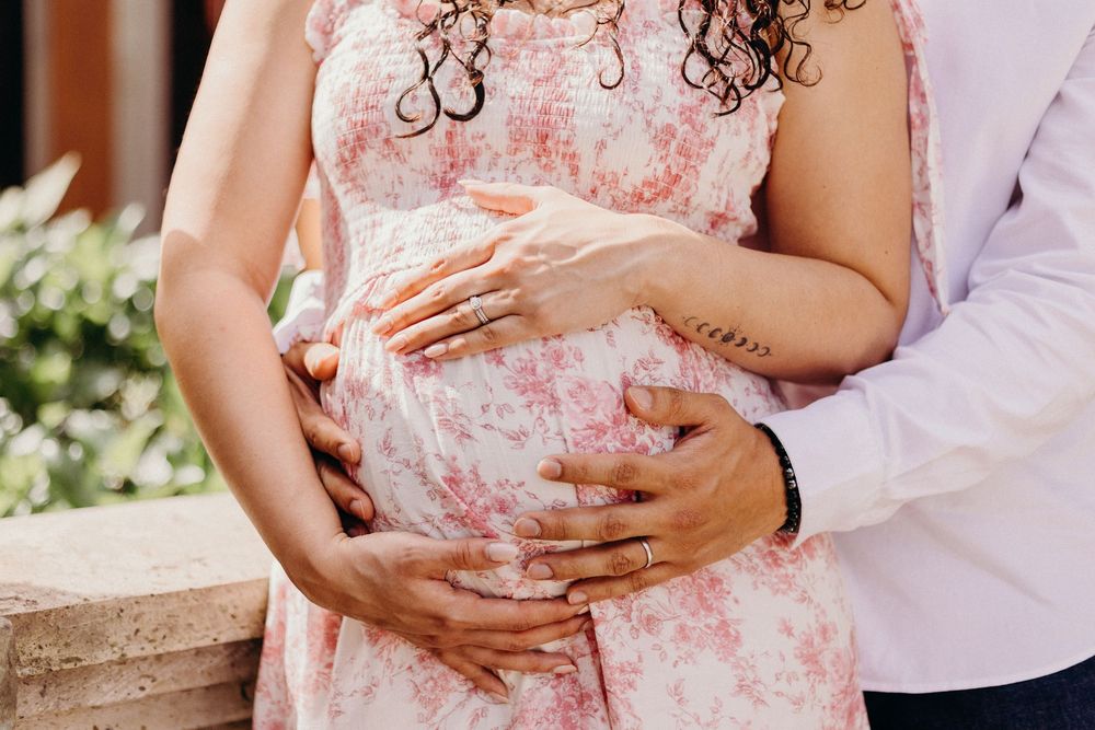 Romantic maternity photos featuring floral dress and gentle embraces in outdoor setting.