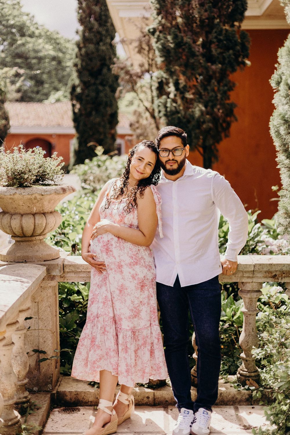 Romantic garden photoshoot with stone urns and floral dress against terracotta wall.