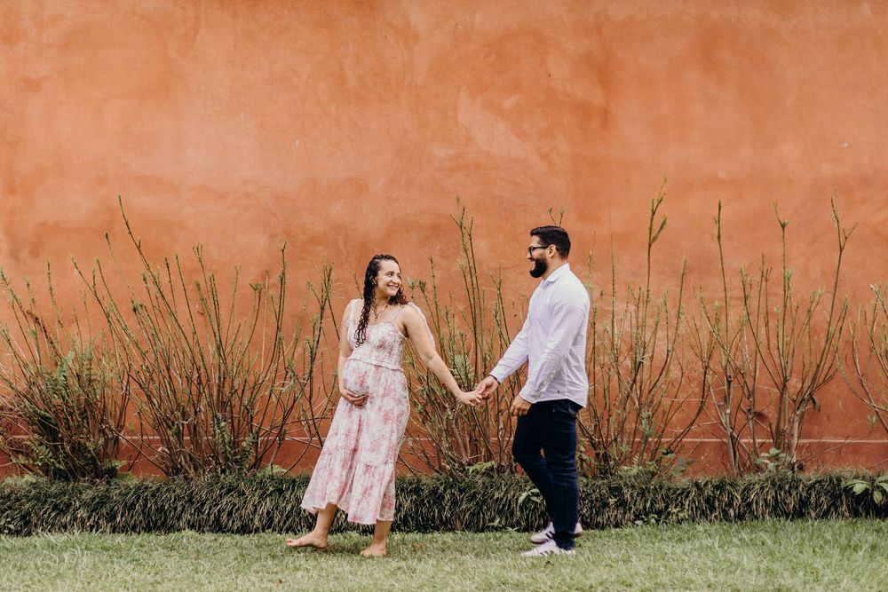A romantic maternity photoshoot against an orange stucco wall outdoors.