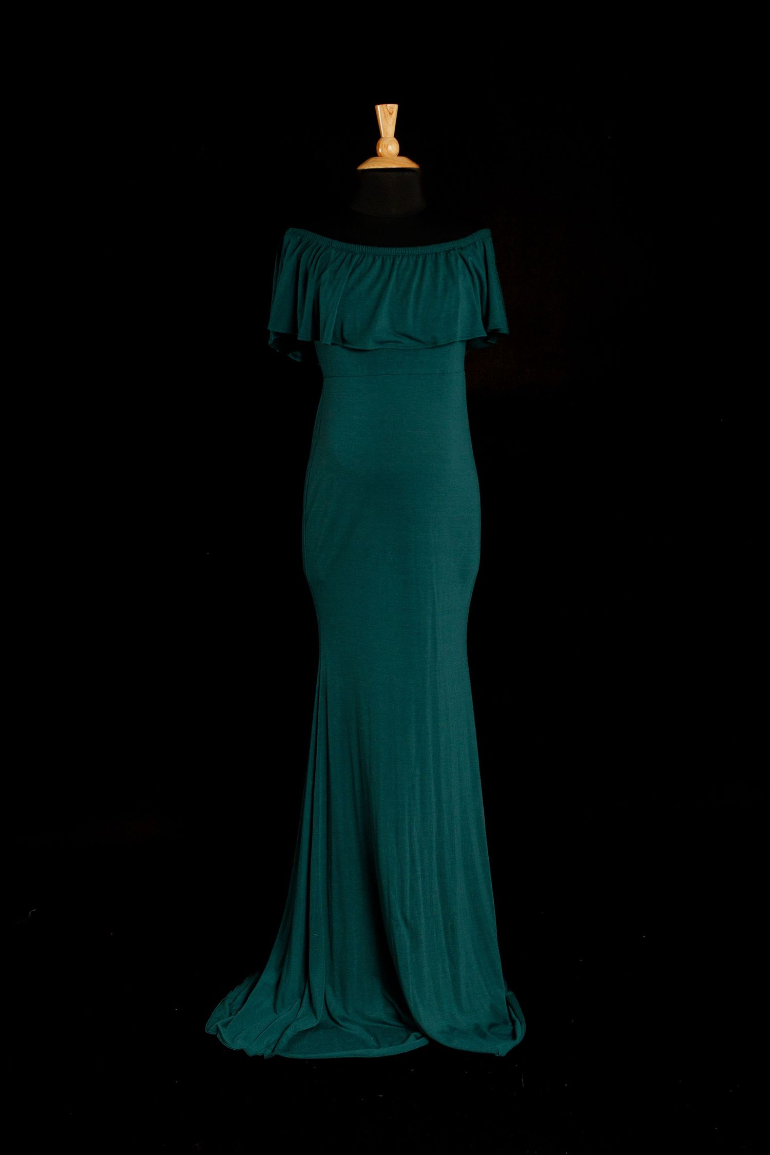Teal green off-the-shoulder fitted maternity gown with ruffle neckline on mannequin.