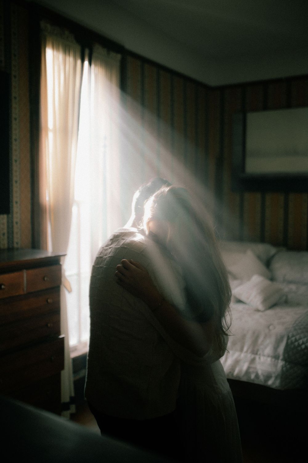 Moody bedroom scene with sunlight streaming through curtains creating dramatic shadows.