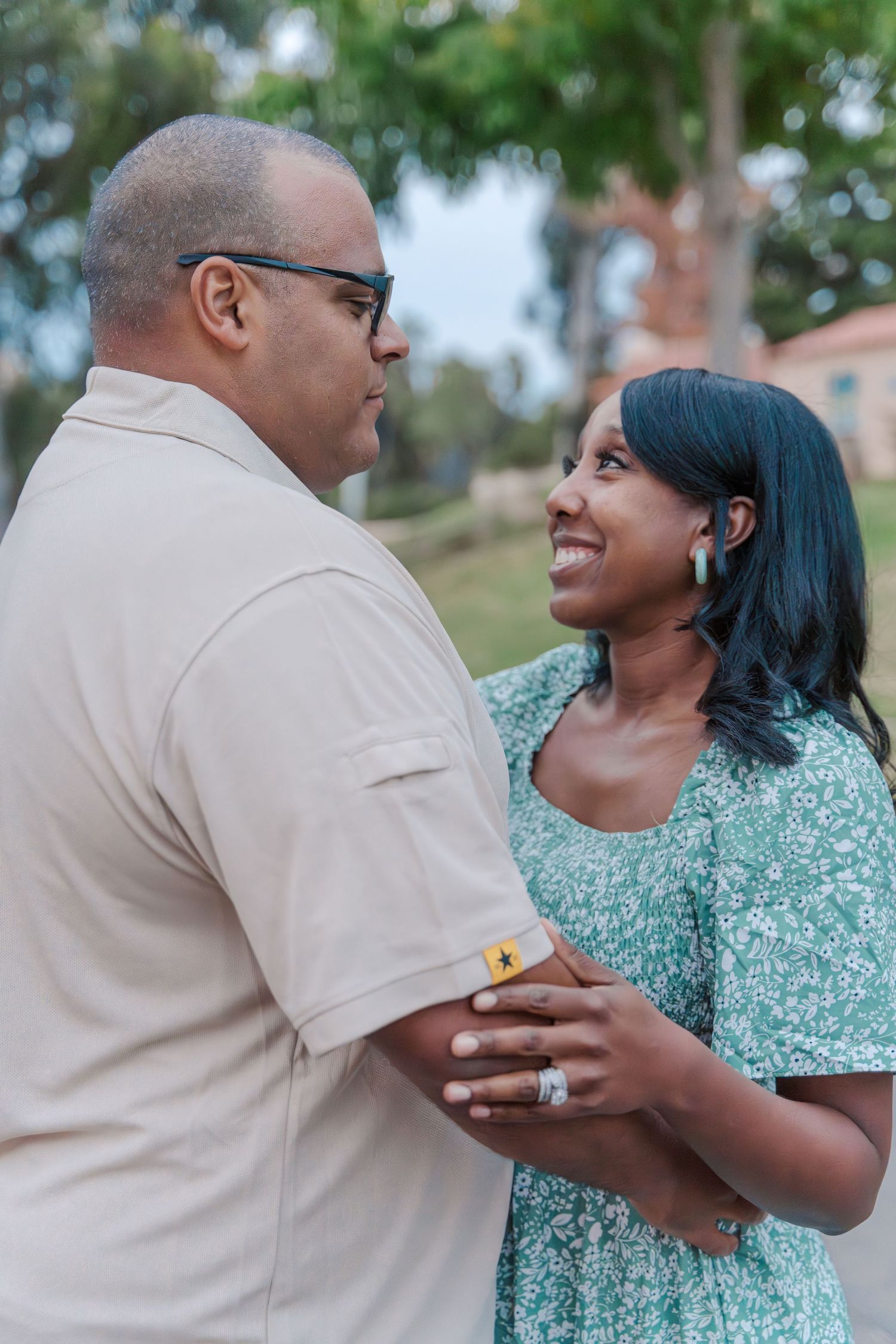 A couple shares an intimate moment outdoors, with the woman wearing a mint green dress and the man in a beige shirt.