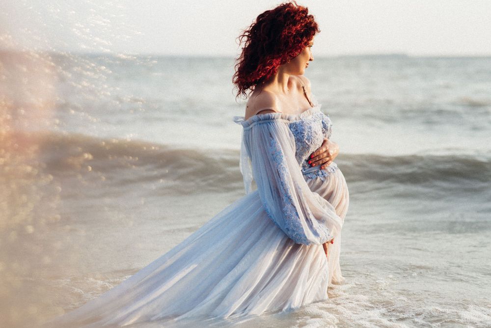 Ethereal beach photoshoot featuring flowing blue dress against ocean waves at sunset.