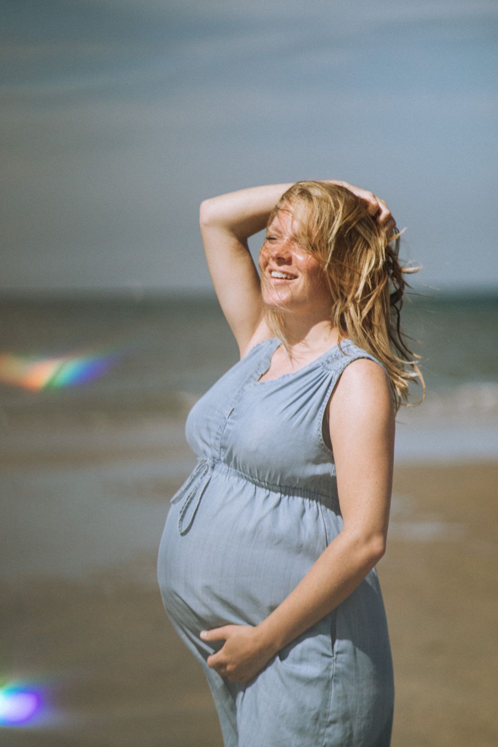 Joyful beach maternity session with lens flare and natural lighting.
