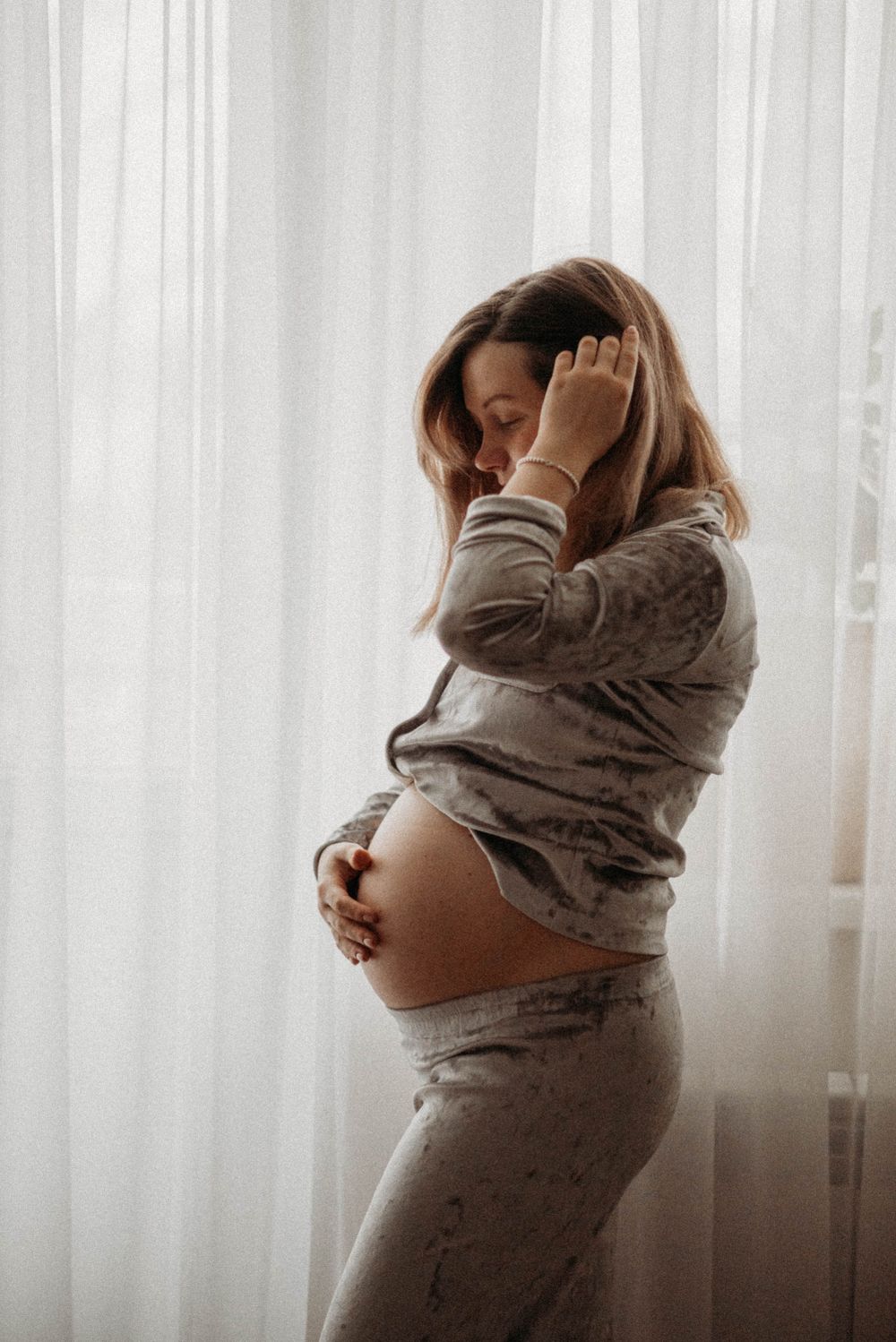 Maternity photoshoot with soft window light and flowing fabric wraps.