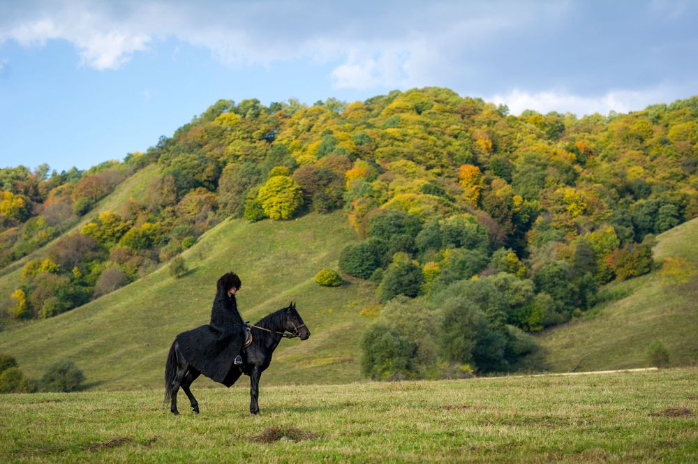 A rider on horseback silhouetted against autumn-colored hillside in golden afternoon light.