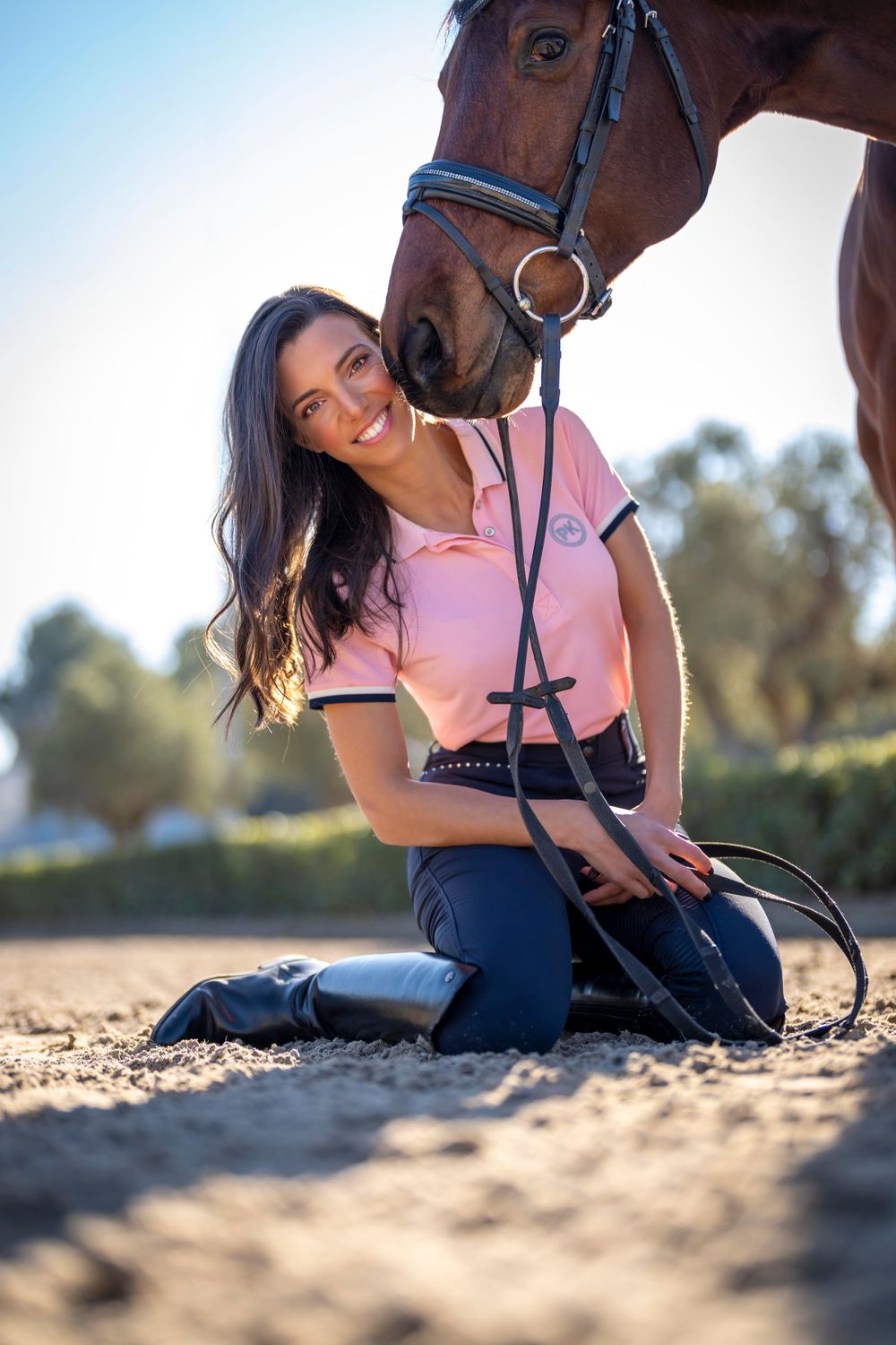 Brown horse with bridle posing with rider in pink shirt outdoors.