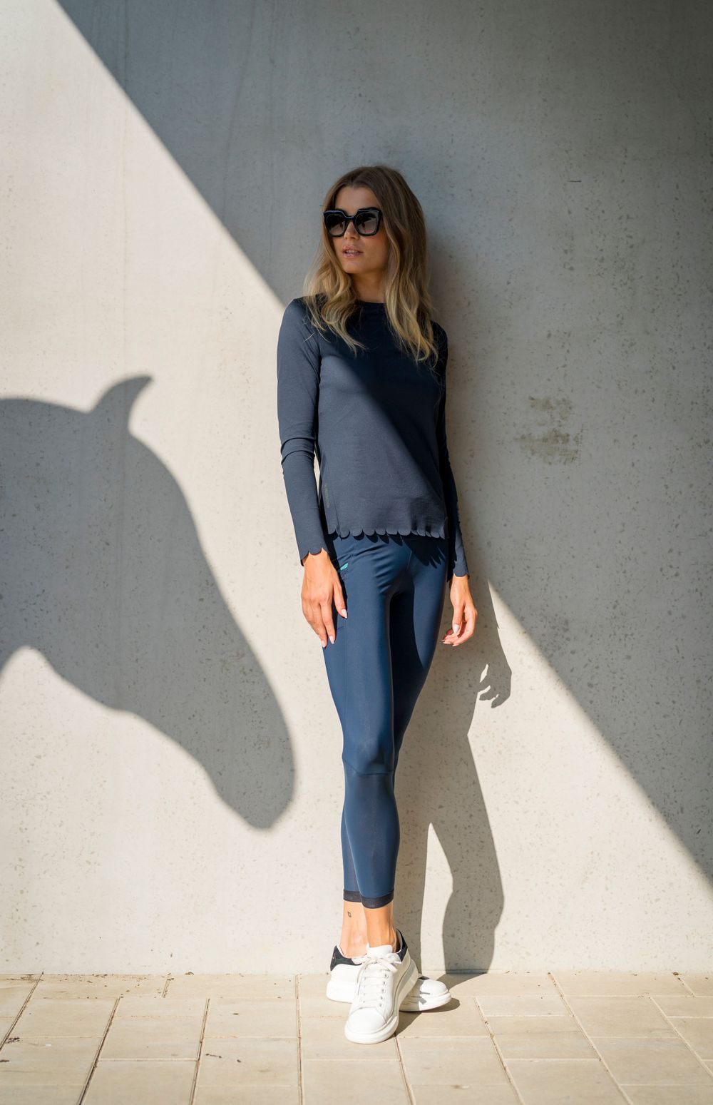 Woman in navy outfit stands against white wall casting dramatic horse shadow.