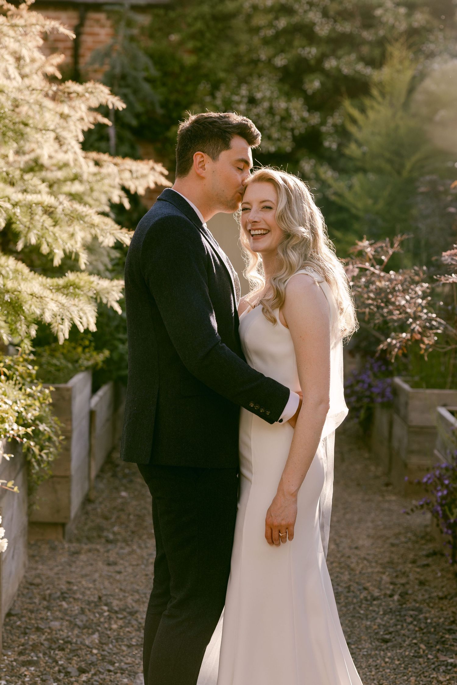 Laughing bride and groom stand together in sunlit garden in grounds of Shortflatt Tower during summer wedding