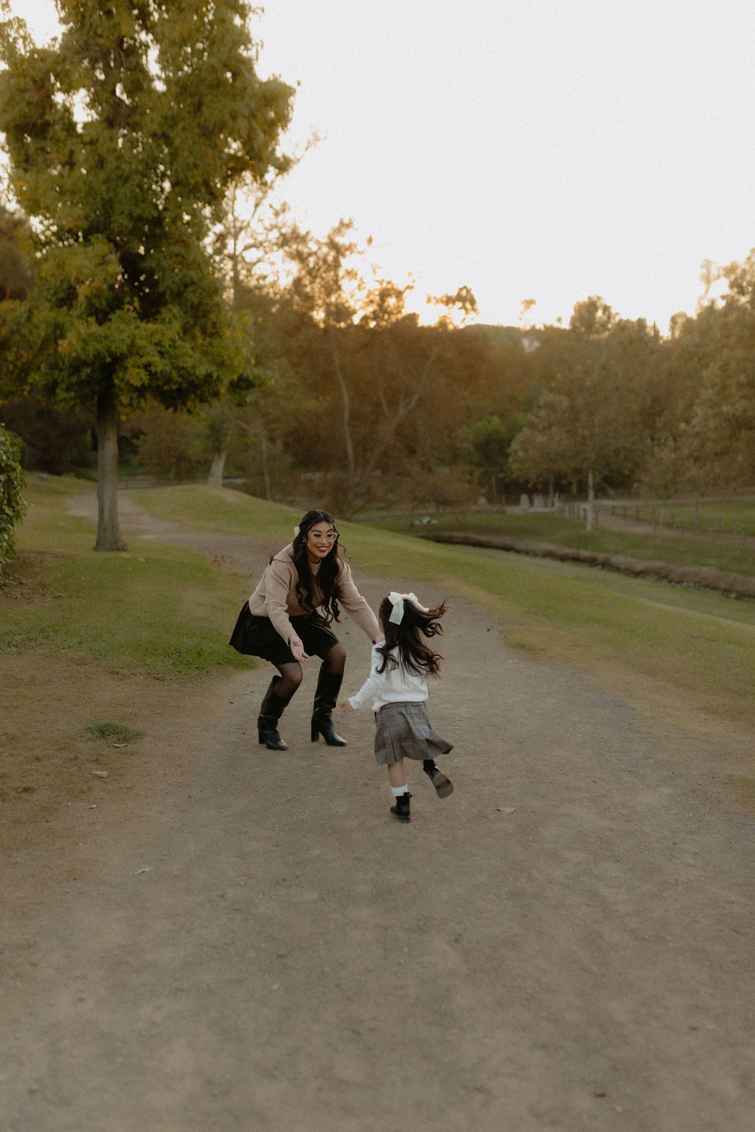 Parent and child playing together on a dirt path in a park at dusk.