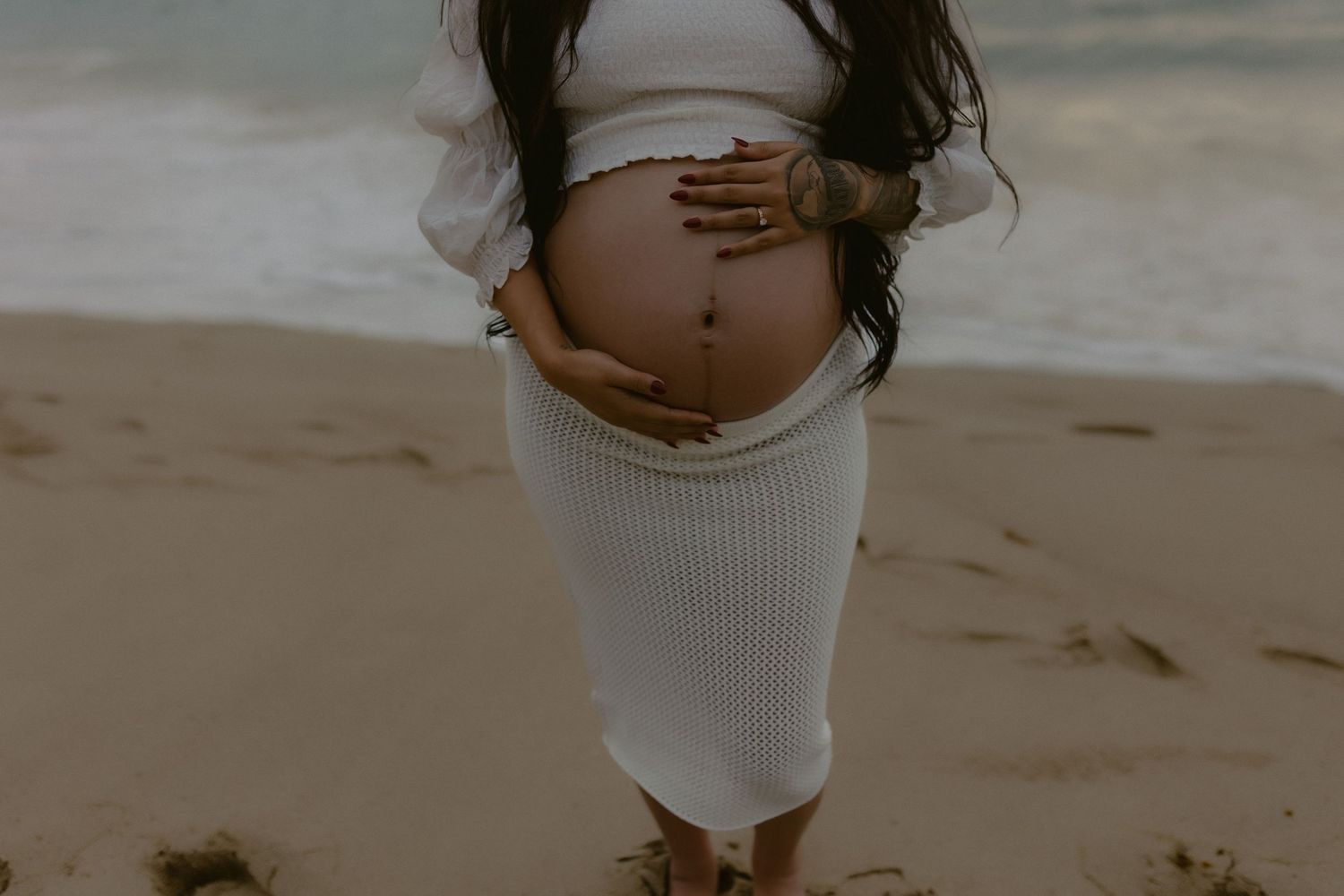 Intimate maternity photo showing hands cradling a pregnant belly on a beach.