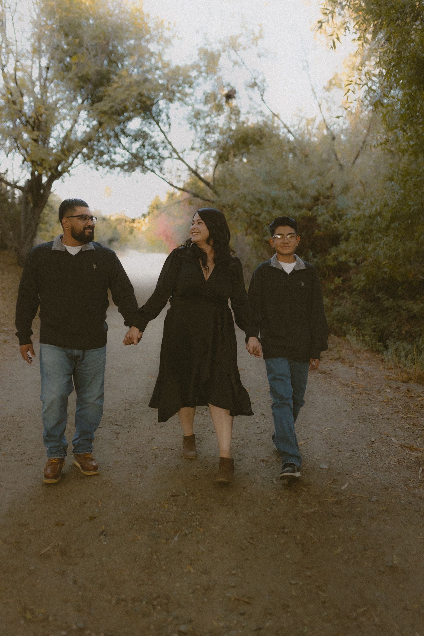 Family of three walking hand in hand on a dirt path during golden hour.