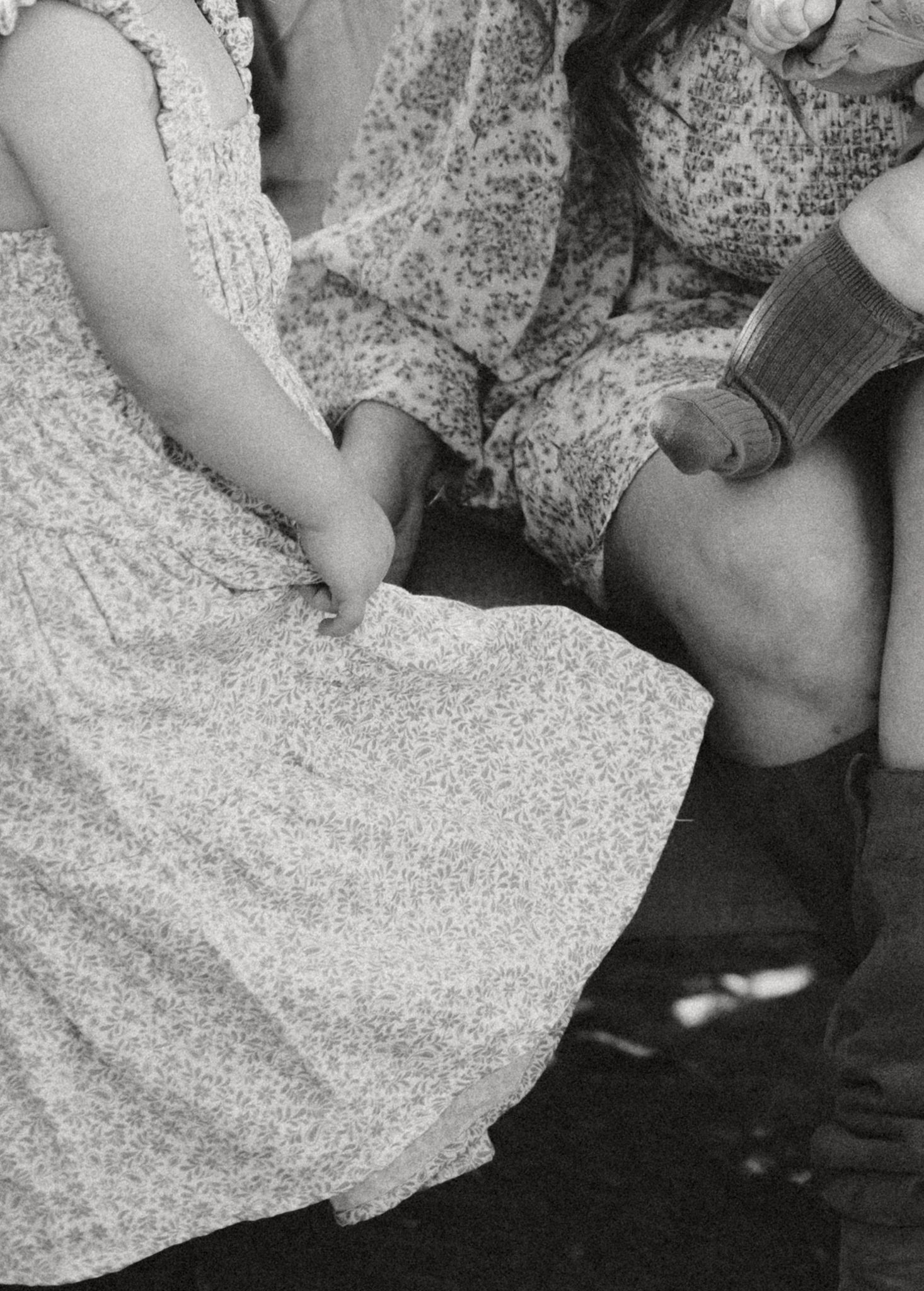 Black and white detail shot of floral dresses and hands creating an intimate moment.