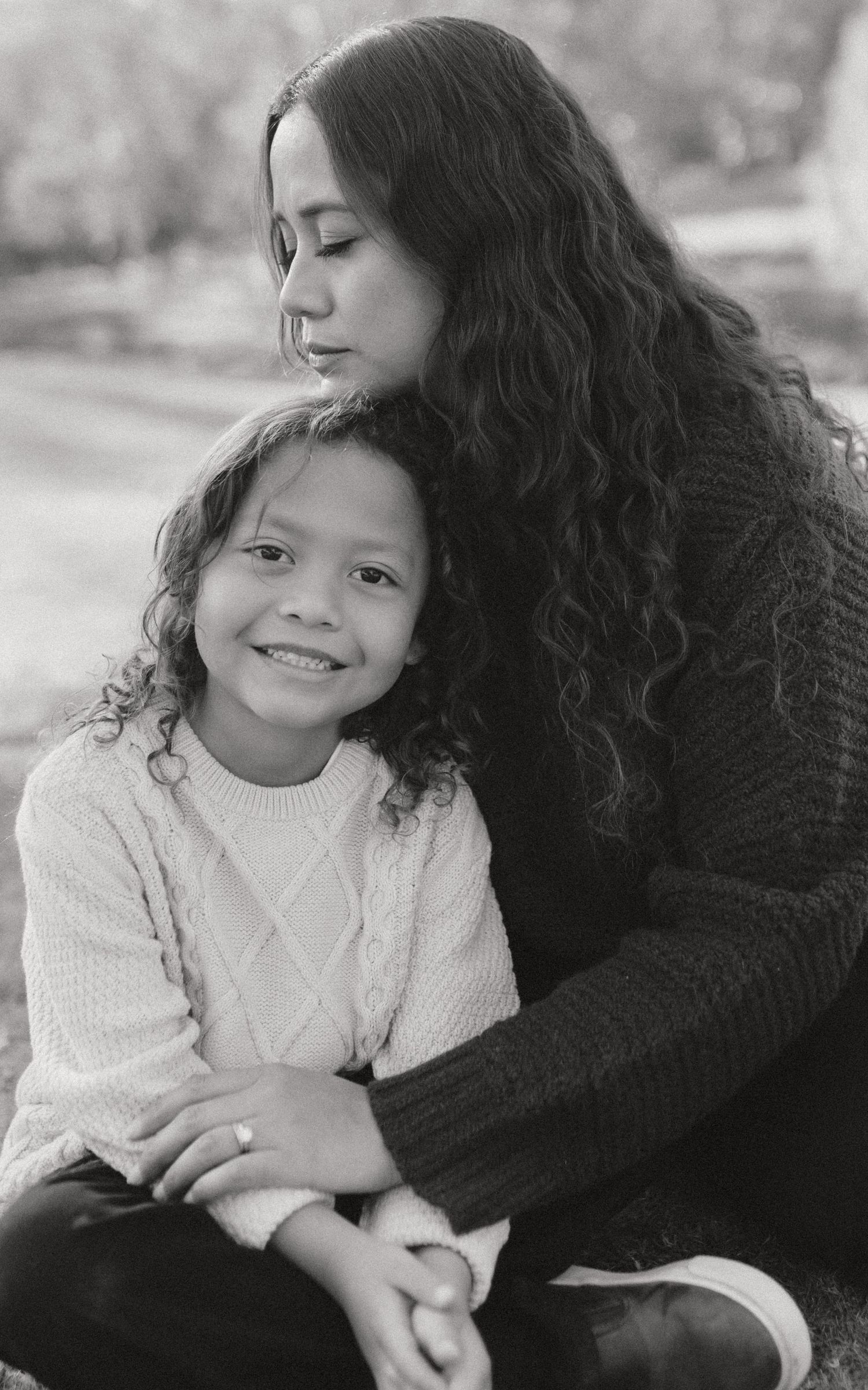 A black and white portrait of a mother and child with curly hair sitting together in an intimate embrace.