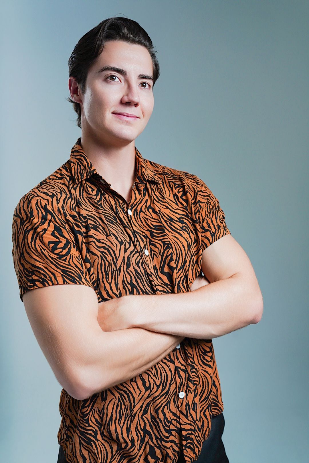 Man in tiger print short sleeve shirt poses against light backdrop.