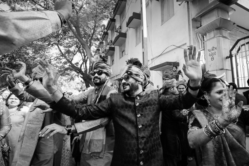 A black and white photo capturing energetic celebration moments at a wedding with dancing and cheering.