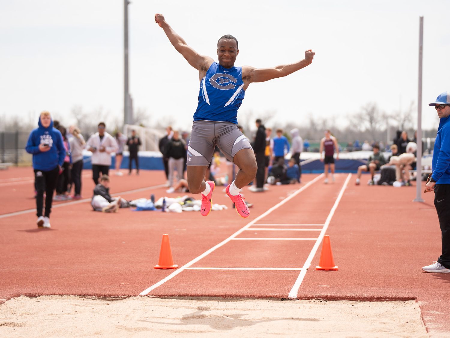Track athlete performs long jump at outdoor competition with orange cones marking the runway.