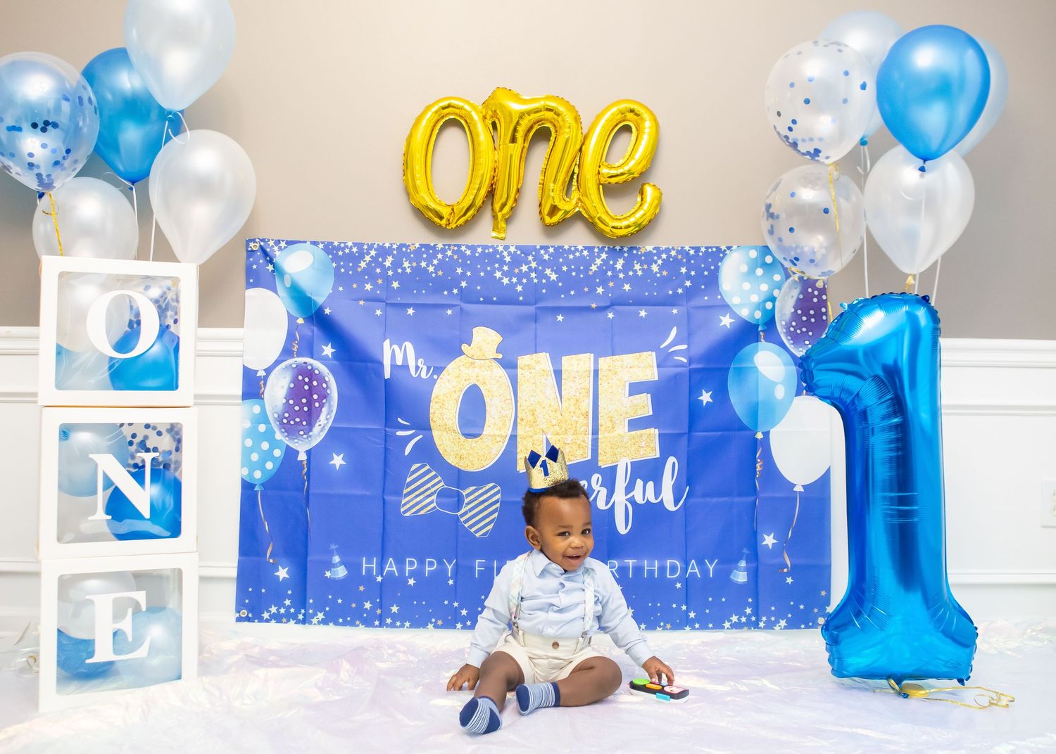 Blue and gold themed first birthday party setup with balloons, decorative backdrop and ONE letter blocks.
