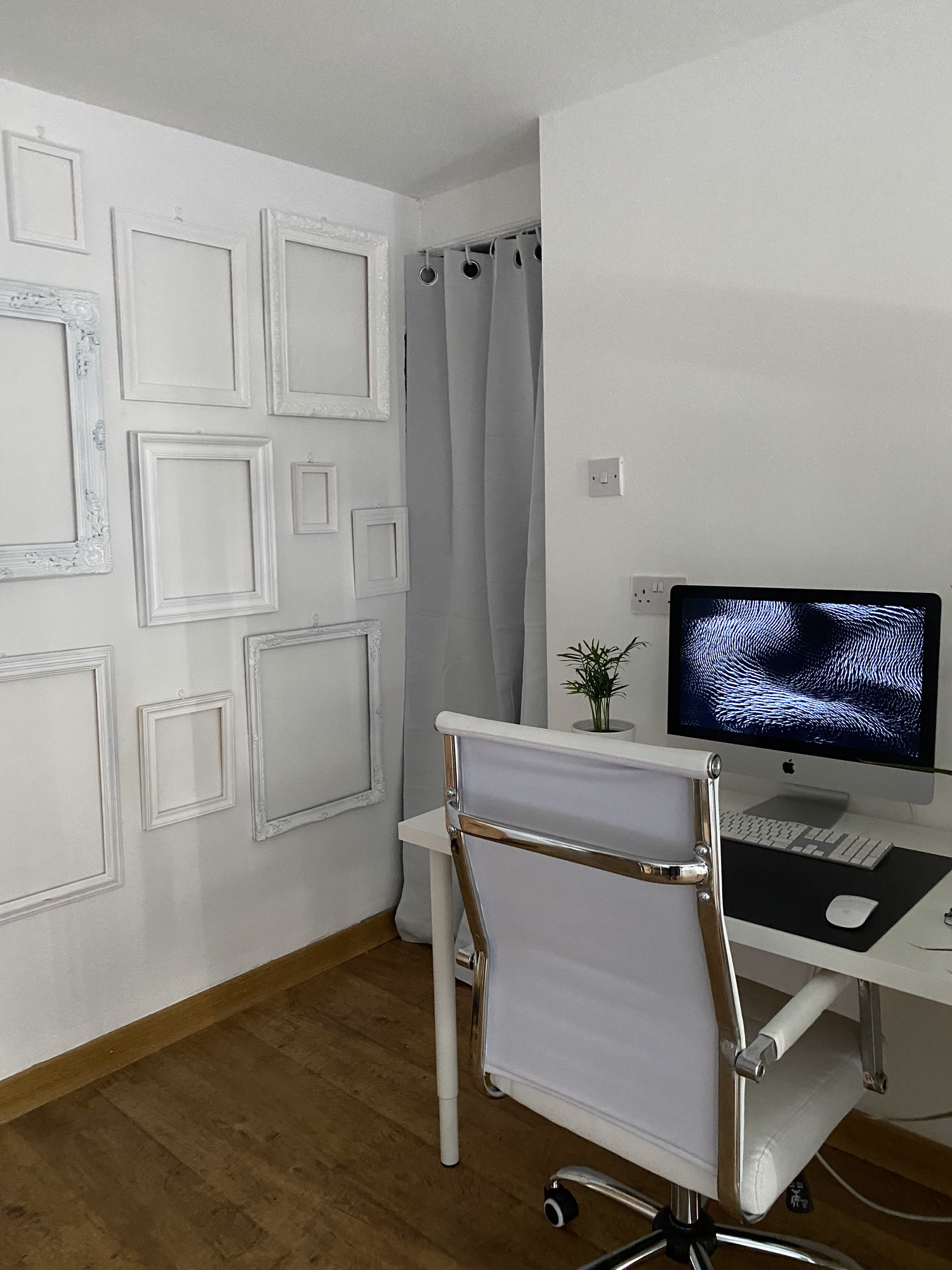 Modern home office setup with iMac computer, white desk chair, and decorative empty frame gallery wall arrangement.