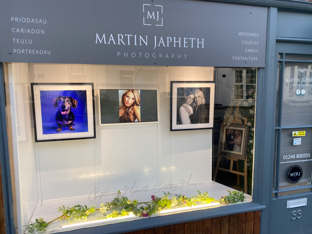 Photography studio window display showcases three framed portrait photos above a planter box with greenery.