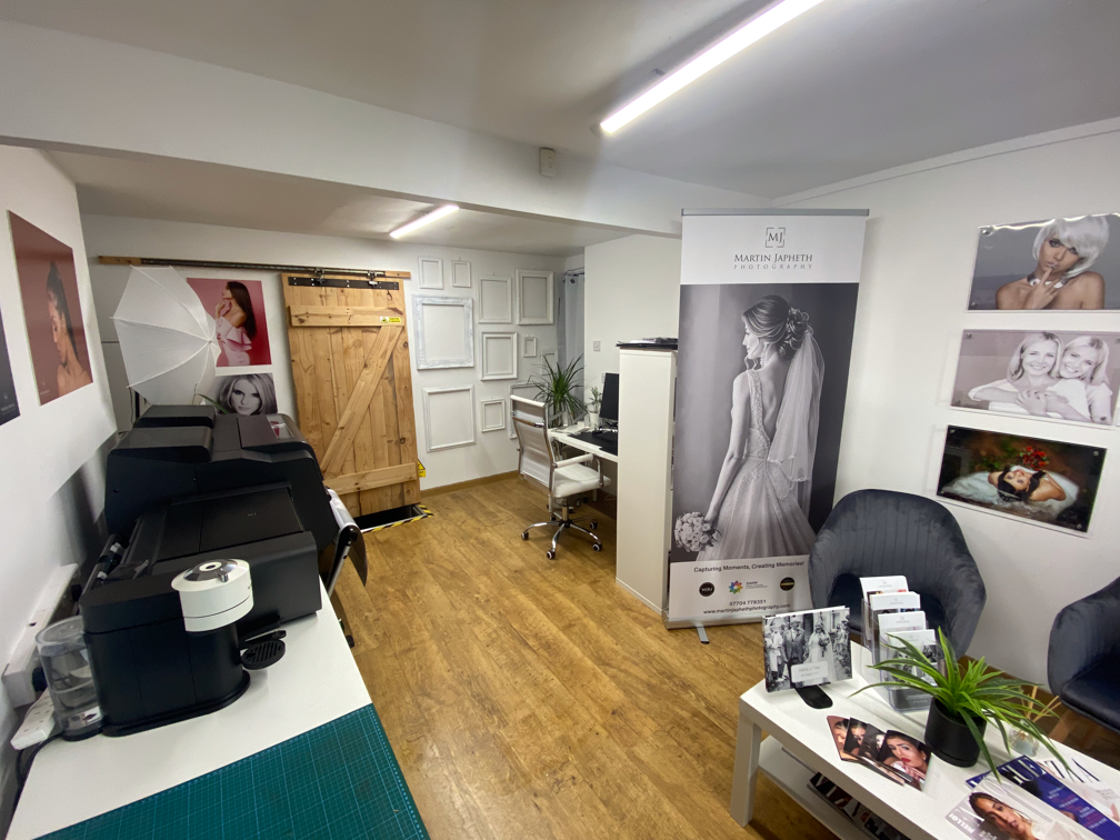 A small studio space with wooden floors, photography equipment, a barn door, and black and green furniture.