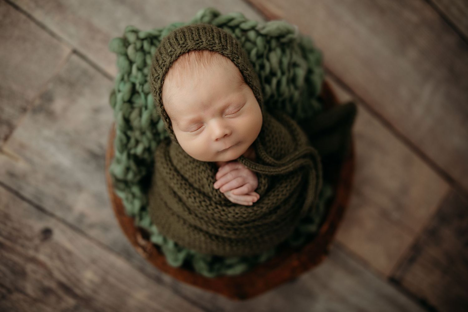 Sleeping infant wrapped in green knit blanket on wooden surface.