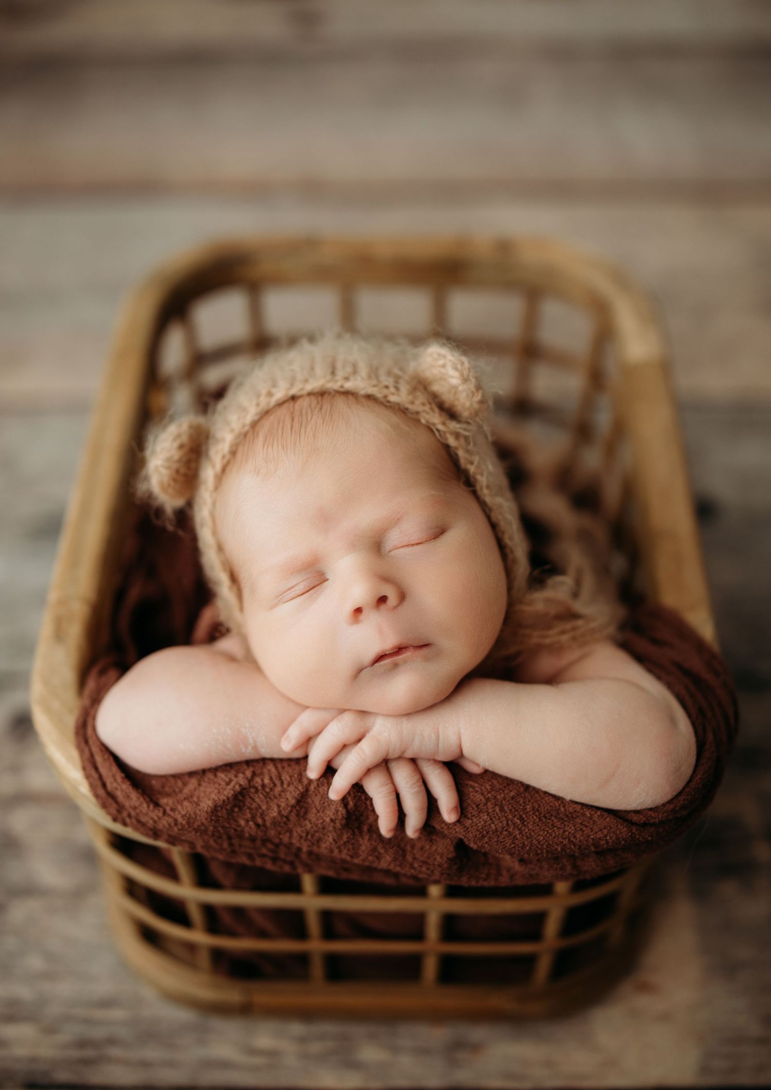 Newborn baby sleeping peacefully in brown woven basket with soft bedding.
